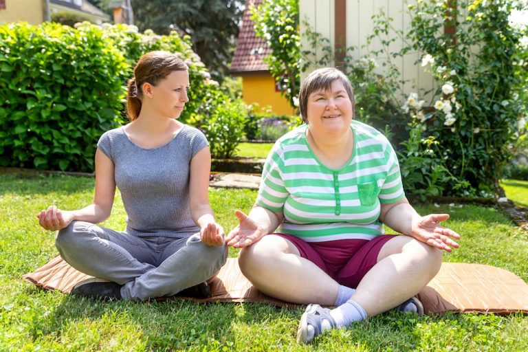 two women, one of them a fitness or yoga coach, are doing some yoga or relaxation exercises, on woman is mentally disabled